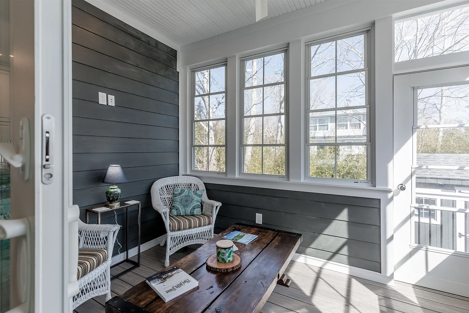 Sunlit porch with wicker chairs and wood table.