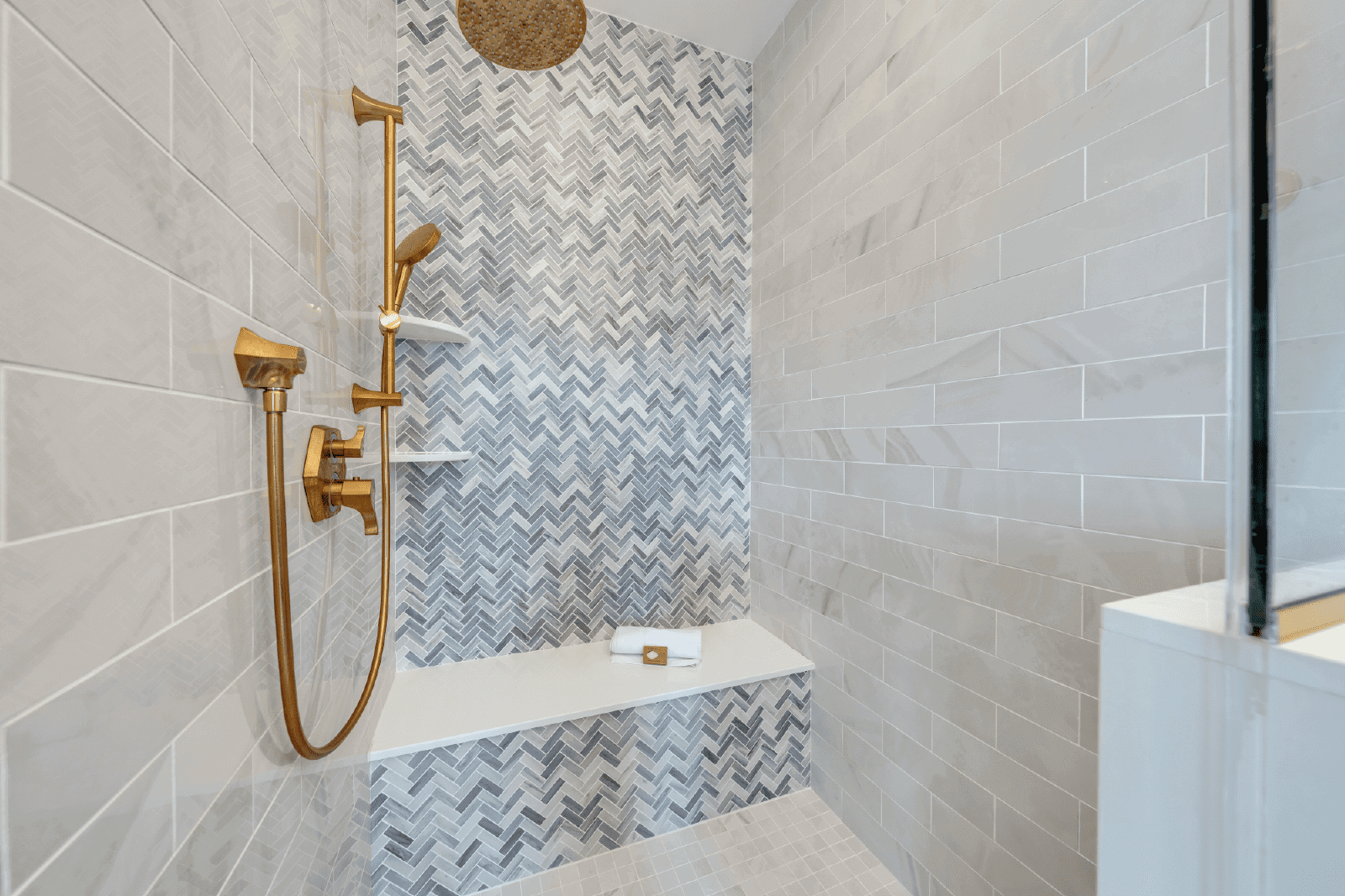 Modern shower with gold fixtures and herringbone tile.